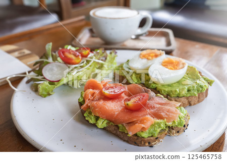 Delicious toasts with avocado, smoked salmon, eggs and a variety of fresh vegetables are served on a rustic plate. A healthy and hearty breakfast in an outdoor cafe. 125465758
