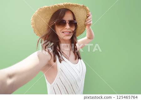 Woman 30- 35 years old female tourist traveler in a wide-brimmed hat takes a selfie against a light green background portrait isolated. The concept of solo travel or advertising summer tours. Woman 30- 35 years old female tourist traveler in a wide-brimmed hat takes a selfie against a light green background portrait isolated. The concept of solo travel or advertising summer tours. 125465764