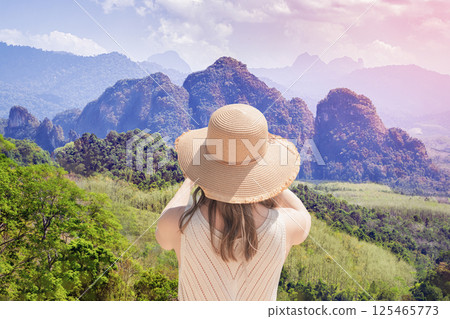 A Woman female traveler shoots a rainforest on a sunny day, rear view from the back. Panorama of the mountains of Khao Sok National Park, view from the observation deck. A Woman female traveler shoots a rainforest on a sunny day, rear view from the back. Panorama of the mountains of Khao Sok National Park, view from the observation deck. 125465773