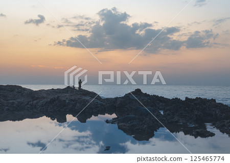 Seascape in Thailand kaolak. Rocky coastal ridge on the background of sunset, panorama. A small silhouette of a fisherman on the rocks. Seascape in Thailand kaolak. Rocky coastal ridge on the background of sunset, panorama. A small silhouette of a fisherman on the rocks. 125465774