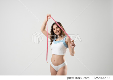 Smiling woman holding measuring tape in fitness studio 125466382