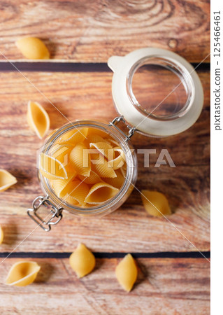 Raw uncooked dried Conchiglie shell pasta. Italian seashells pasta in lock lid jar on wooden background. 125466461