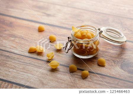 Raw uncooked dried Conchiglie shell pasta. Italian seashells pasta in lock lid jar on wooden background. 125466463