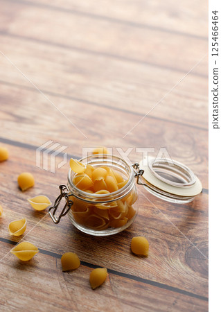 Raw uncooked dried Conchiglie shell pasta. Italian seashells pasta in lock lid jar on wooden background. 125466464