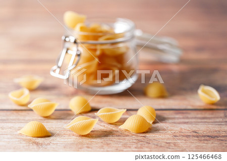 Raw uncooked dried Conchiglie shell pasta. Italian seashells pasta in lock lid jar on wooden background. 125466468
