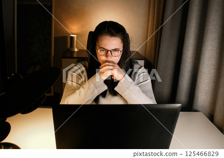 Young woman with eyeglasses working on laptop at home late at night, using modern technologies and getting online education. Remote learning concept. Online university. Focus on process. Young woman with eyeglasses working on laptop at home late at night, using modern technologies and getting online education. Remote learning concept. Online university. Focus on process. 125466829