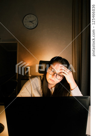 Woman working on laptop late evening at home. Concentrated female employee solves work issues sitting at computer at work desk. Woman working on laptop late evening at home. Concentrated female employee solves work issues sitting at computer at work desk. 125466836