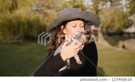 A delightful and joyful moment captured of a woman affectionately kissing her small dog while outdoors 125468610