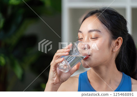 Active woman enjoying a refreshing drink, promoting hydration and wellness in a modern setting. Active woman enjoying a refreshing drink, promoting hydration and wellness in a modern setting. 125468891
