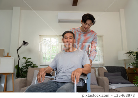 Son assisting elderly father in a wheelchair within a bright living room. Son assisting elderly father in a wheelchair within a bright living room. 125468978