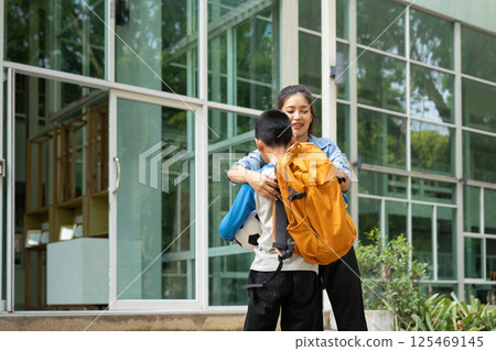 Family Support and School Arrival. A mother helps her son get ready for school while holding his backpack and soccer ball. 125469145