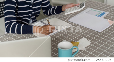 Person organizing finances with notebook and calculator at home Person organizing finances with notebook and calculator at home 125469296