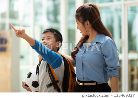 Joyful Journey to School. A mother and son enjoying a moment as they head to school with a soccer ball. Joyful Journey to School. A mother and son enjoying a moment as they head to school with a soccer ball. 125469327