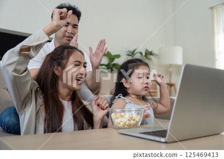 Family celebrating together while watching a movie on a laptop, sharing popcorn and excitement. Family celebrating together while watching a movie on a laptop, sharing popcorn and excitement. 125469413