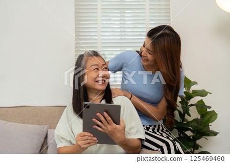 Wellness and Modern Living. A mother and daughter share a light-hearted moment while using a tablet together. 125469460