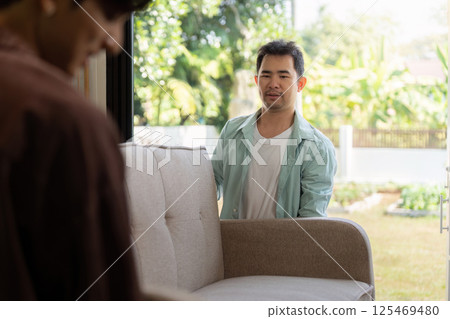 Couple moving house together, a gay couple happily carrying a sofa into their new home 125469480