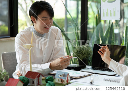 Sustainable Solutions and Innovation. A young professional discusses eco-friendly architecture with a colleague in an office setting. 125469510