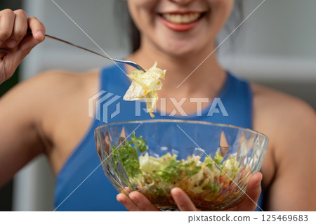 Close-up of a woman smiling while holding a forkful of salad, highlighting healthy eating. 125469683