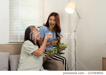 Healthy Eating and Joyful Moments. A mother and daughter savoring salad in a relaxed home setting. 125469691