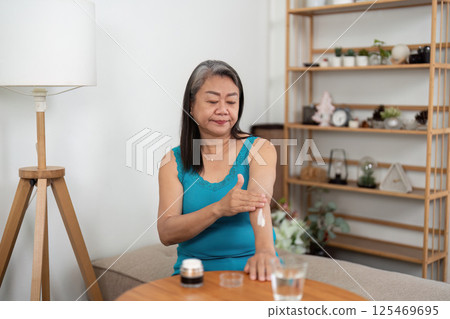 Beauty and Wellness. An elderly woman applying lotion on her arm, embracing self-care in a cozy home setting. Beauty and Wellness. An elderly woman applying lotion on her arm, embracing self-care in a cozy home setting. 125469695