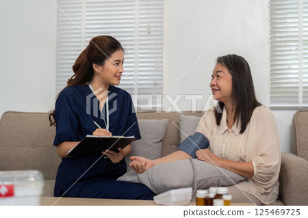 Caregiving and Health Monitoring. A caregiver takes notes while consulting with an elderly woman about her health. 125469725