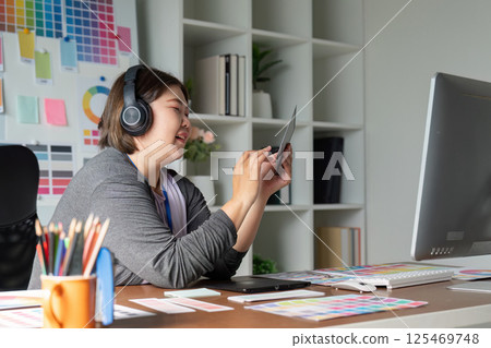 Graphic designer engaged in digital design work while wearing headphones in a modern creative workspace 125469748