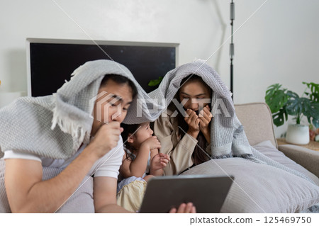 Cozy Family Moments and Screen Time. A family watches a film under a shared blanket, sharing laughs and popcorn. 125469750