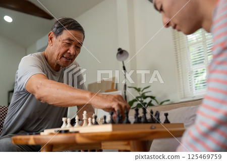 Father smiling while making a chess move against his son at home. 125469759