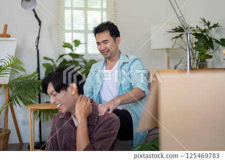 LGBTQ couple sharing a laugh during a massage while settling into their new home. LGBTQ couple sharing a laugh during a massage while settling into their new home. 125469783