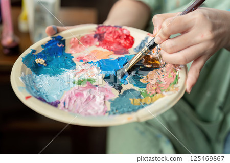 Young artist mixing vibrant colors on a palette with a brush, showcasing creativity and artistic expression 125469867