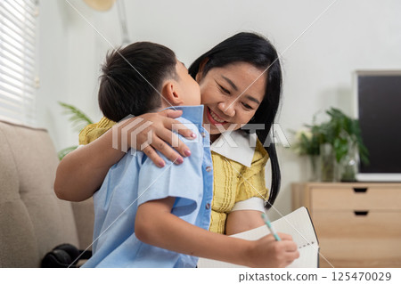 Mother and Son Bonding Over Homework. A mother and son share a loving moment while working on school assignments. 125470029