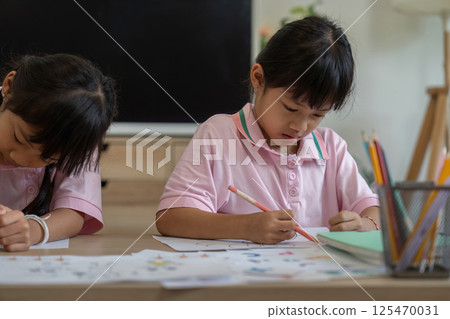 Focused Learning and Creativity. Two girls deeply engaged in their coloring projects at home. 125470031
