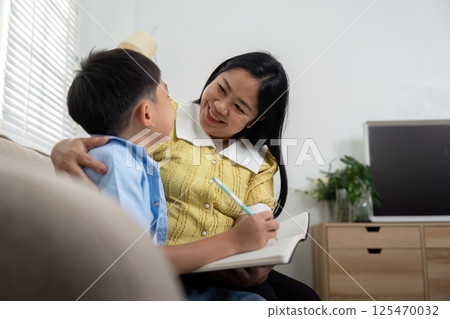 Mother and Son Learning Together. A mother joyfully assists her son with his studies, creating a nurturing atmosphere. 125470032