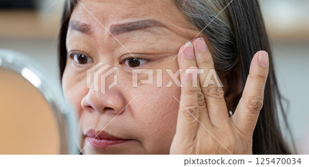 Beauty and Wellness. A senior woman applying cream around her eyes for skincare. 125470034