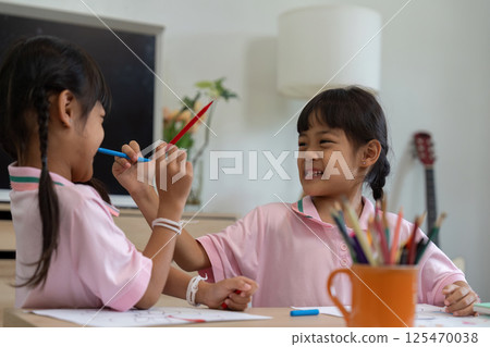 Playfulness and Fun. Two girls enjoying a playful moment with colored pencils. 125470038