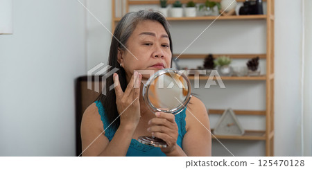 Beauty and Wellness. An elderly woman examining her skin in a mirror, focusing on self-care. 125470128
