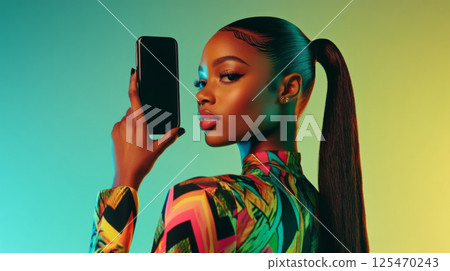 Stylish woman holding a smartphone against teal background 125470243