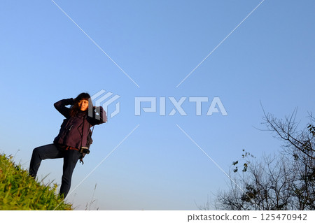 Traveler Asian woman wearing jacket and hood standing on green lawn grass and blue sky with sunrise in winter with valley mountain view in Chiangmai Province of Thailand Traveler Asian woman wearing jacket and hood standing on green lawn grass and blue sky with sunrise in winter with valley mountain view in Chiangmai Province of Thailand 125470942