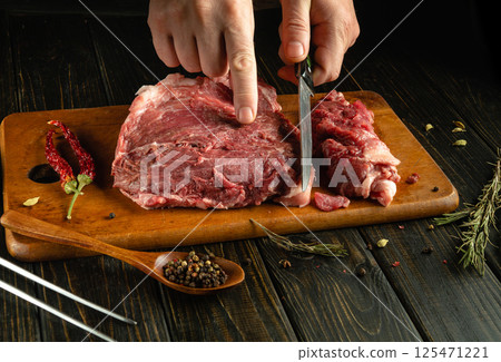 A person skillfully slices raw meat on a wooden cutting board, surrounded by herbs, spices, and a rustic kitchen ambiance, highlighting culinary preparation A person skillfully slices raw meat on a wooden cutting board, surrounded by herbs, spices, and a rustic kitchen ambiance, highlighting culinary preparation 125471221