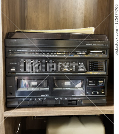 A vintage stereo tape recorder or boombox. The equipment stands on a wooden shelf. A vintage stereo tape recorder or boombox. The equipment stands on a wooden shelf. 125474706