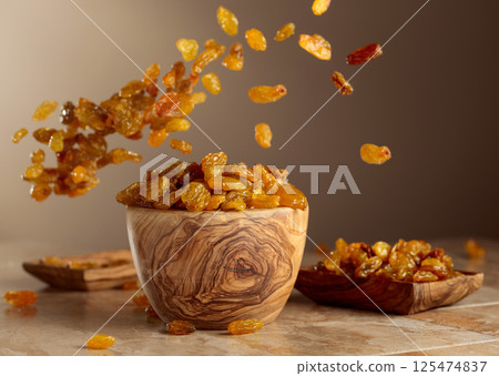 Yellow sultana raisins pour into a wooden bowl. Yellow sultana raisins pour into a wooden bowl. 125474837