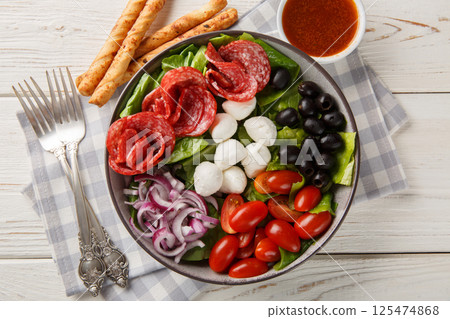 Italian fresh pizza salad with sausages, mozzarella cheese, tomatoes, olives, onions, romaine lettuce and spicy vinaigrette dressing served with breadsticks. Horizontal top view 125474868