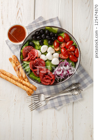 Pizza salad tosses mix of romaine lettuce, sausages, mozzarella, black olives and red onion in a fresh, grated tomato vinaigrette closeup on the plate. Vertical top view 125474870