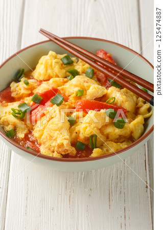 Soft silky eggs stir fried in a sweet tangy tomato sauce with green onions closeup on the plate. Vertical 125474887