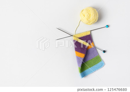 Striped piece of knitted fabric for future clothing with knitting needles and yellow ball of thread on gray background. Homemade needlework and knitting of warm, clothes and toys. Concept creativity Striped piece of knitted fabric for future clothing with knitting needles and yellow ball of thread on gray background. Homemade needlework and knitting of warm, clothes and toys. Concept creativity 125476680