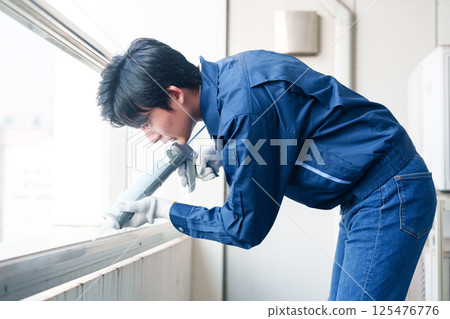 Male worker applying caulking material during exterior construction work 125476776