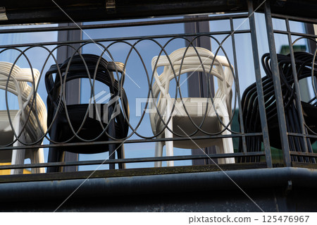 The plastic chairs are folded and stand on the balcony behind the fence 125476967