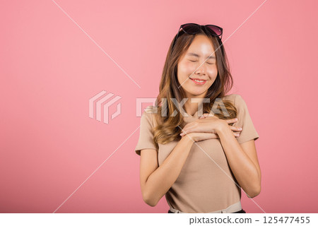 Beauty Asian young woman touching her chest for thanking in studio shot isolated on pink background, happy charming female smiling hold hands chest near heart honest with grateful gesture Beauty Asian young woman touching her chest for thanking in studio shot isolated on pink background, happy charming female smiling hold hands chest near heart honest with grateful gesture 125477455