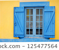 Blue wooden window on a yellow wall 125477564