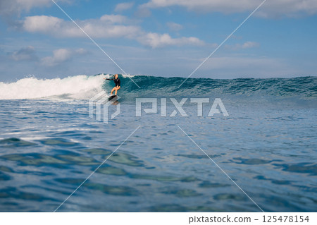 Female surfer riding a perfect swell wave on sunny day, surfing in ocean. 125478154